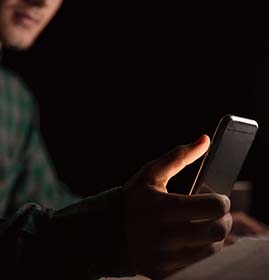 Closeup of man sitting at the table and using cell phone in the dark room